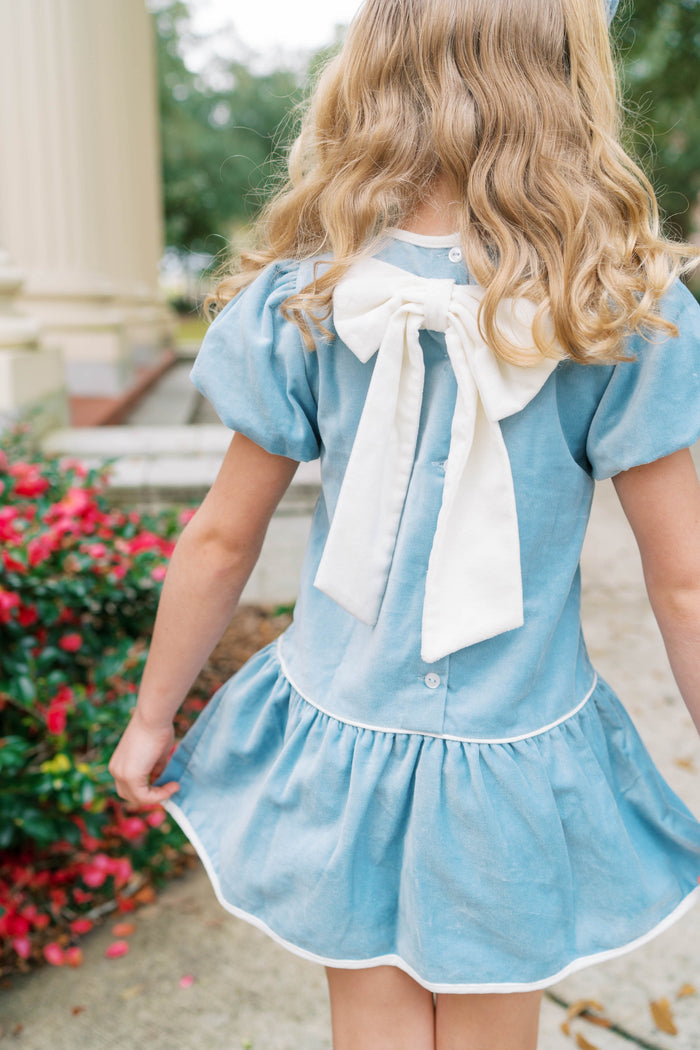 The Harper Dress captures effortless elegance in sumptuous Beaufort blue velvet. Designed for girls ages 5–8, this charming piece features an oversized back bow—a subtle yet striking detail that elevates any occasion. Whether she's attending a fall celebration or holiday gathering, the luxurious velvet drape and thoughtful silhouette make this dress a wardrobe essential. A timeless choice for special moments.